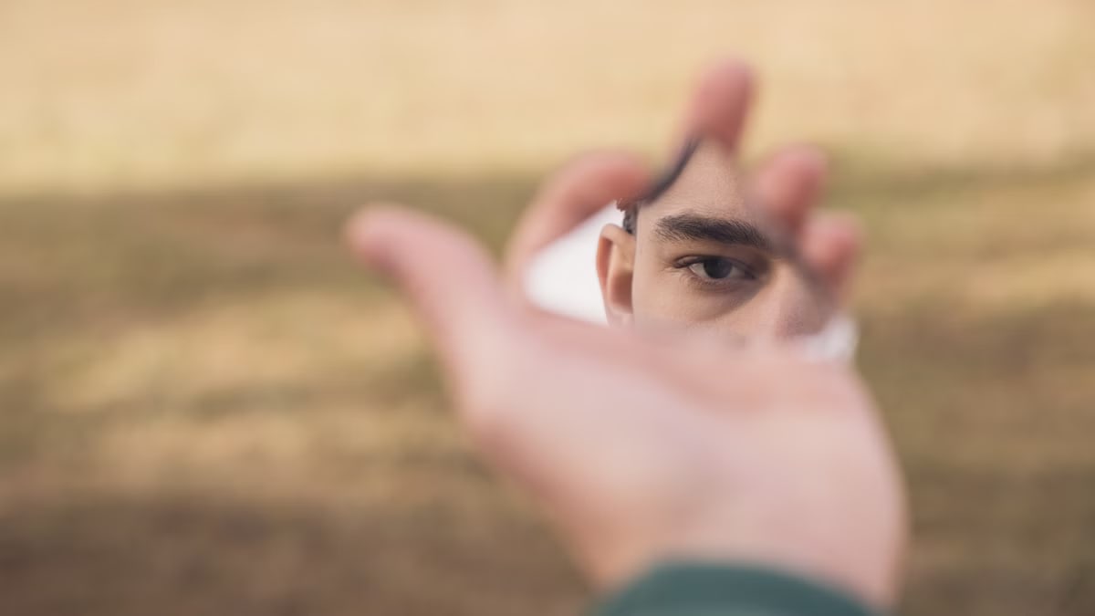 A person's eye reflected in a shard of mirror held outdoors, creating a surreal effect.