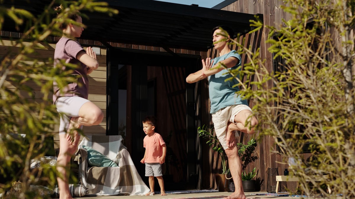 A family practicing yoga in tree pose on a sunlit porch, promoting health and mindfulness.